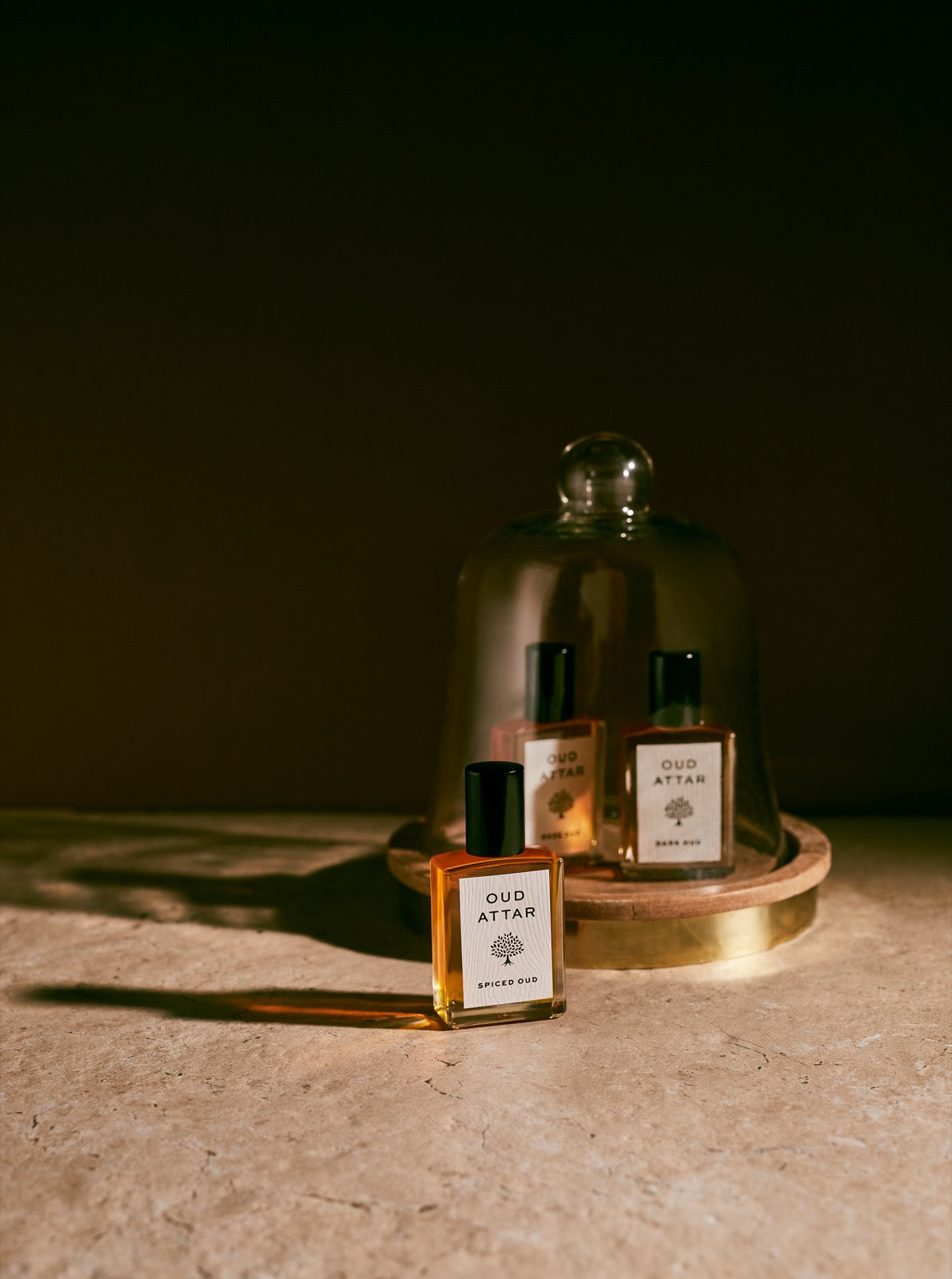 Oud Attar bottles resting under a glass cloche in low light