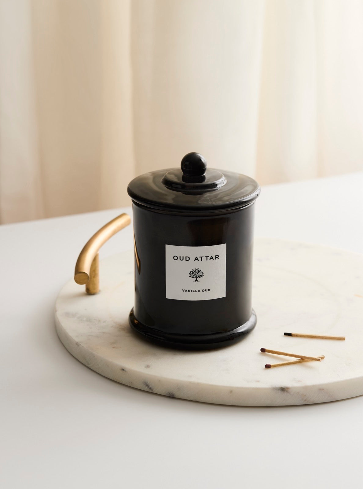 Unlit Vanilla Oud candle beside matches in soft sunlight