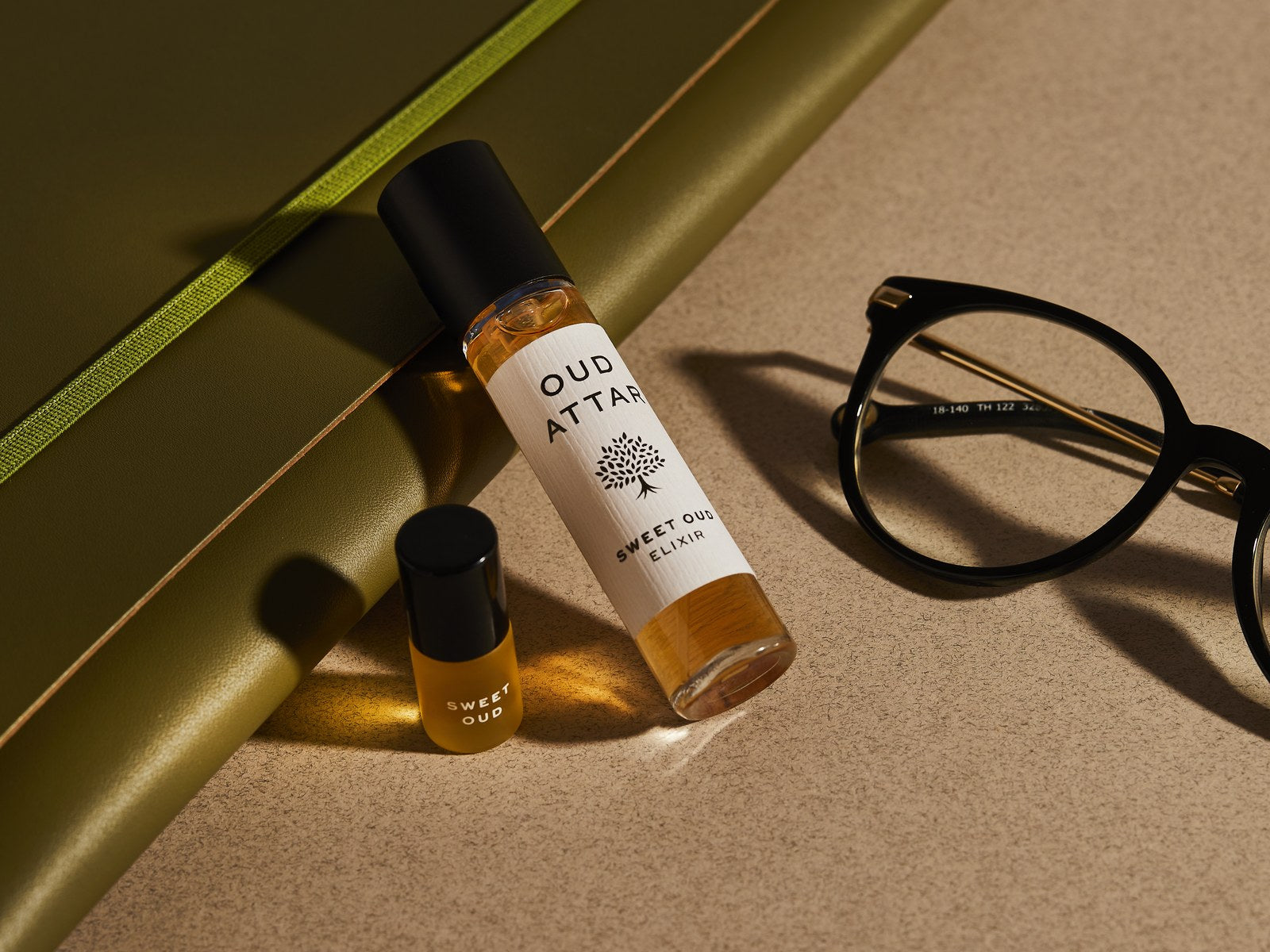 Oud travel set on a green notebook beside glasses
