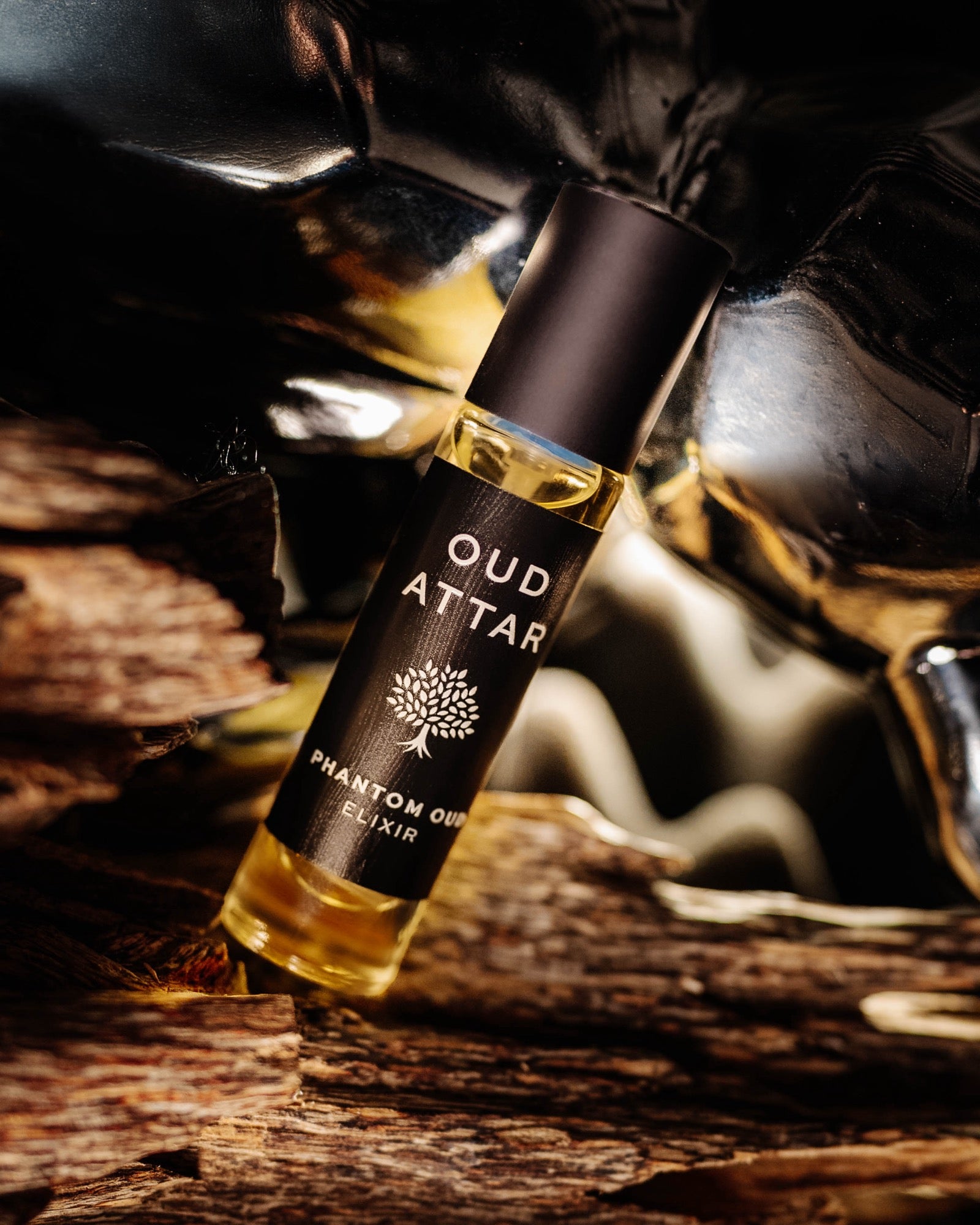 An Oud Attar elixir bottle resting on raw agarwood chips