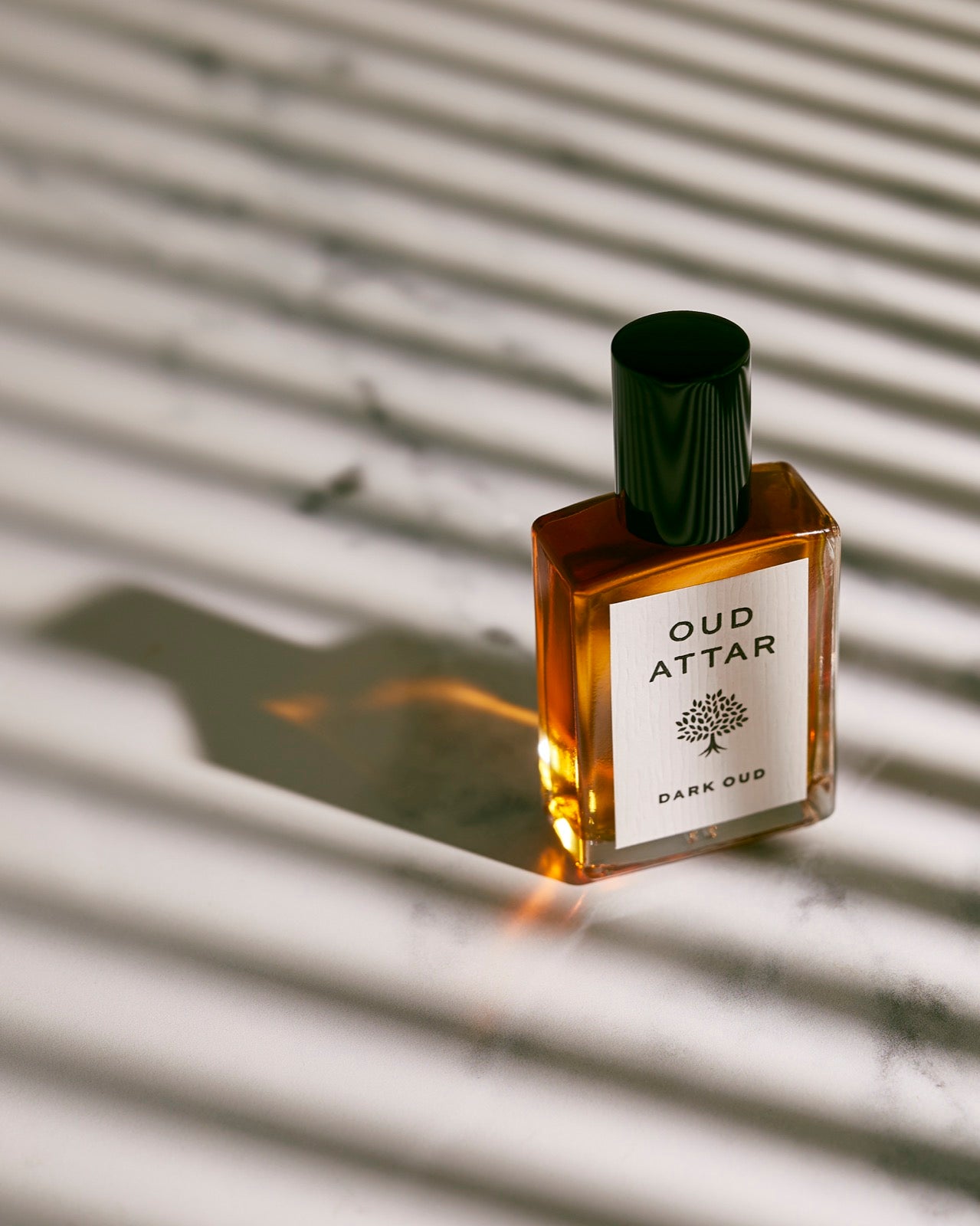 Dark Oud bottle on marble in dramatic window light