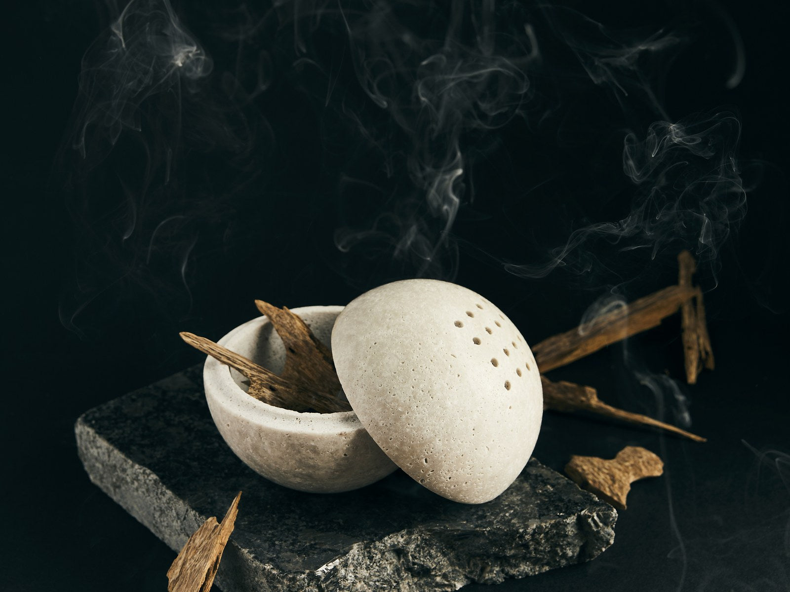 Stone oud burner with rising smoke and agarwood chips