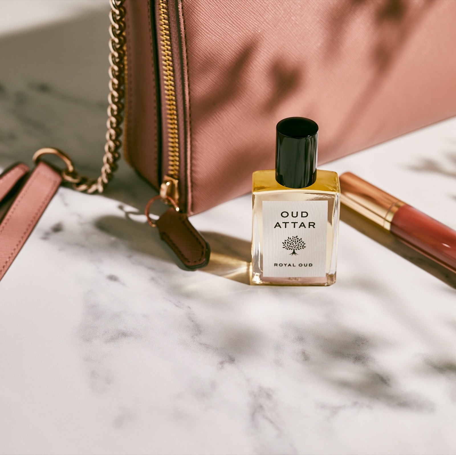 Royal Oud perfume oil on a marble vanity beside a handbag